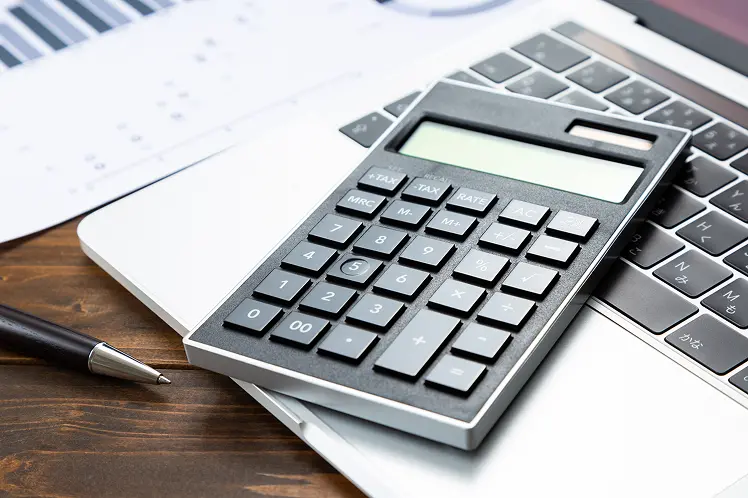 ノートパソコンのキーボードの上に電卓が置かれているビジネスシーン