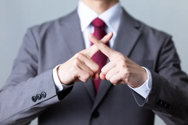 スーツを着た男性が手でバツ印を作り、拒否や否定の意思を示している
